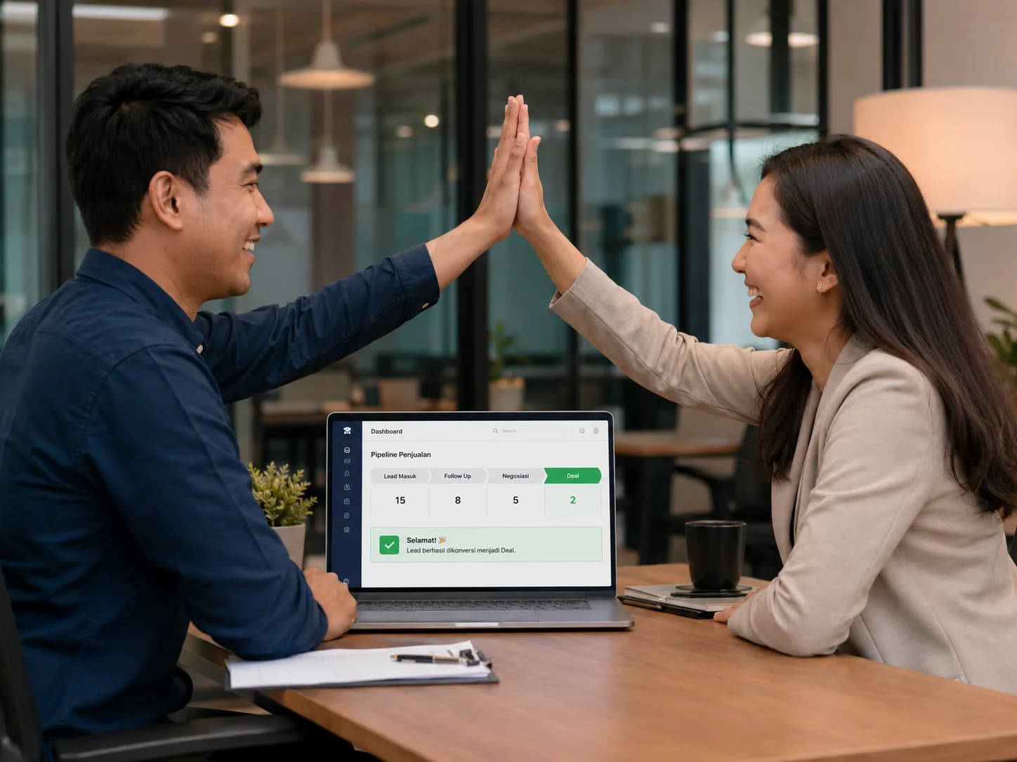 Sales team 2 orang tersenyum high-five di depan laptop menampilkan pipeline dashboard lead deal (Fitur 4 · Manfaat)